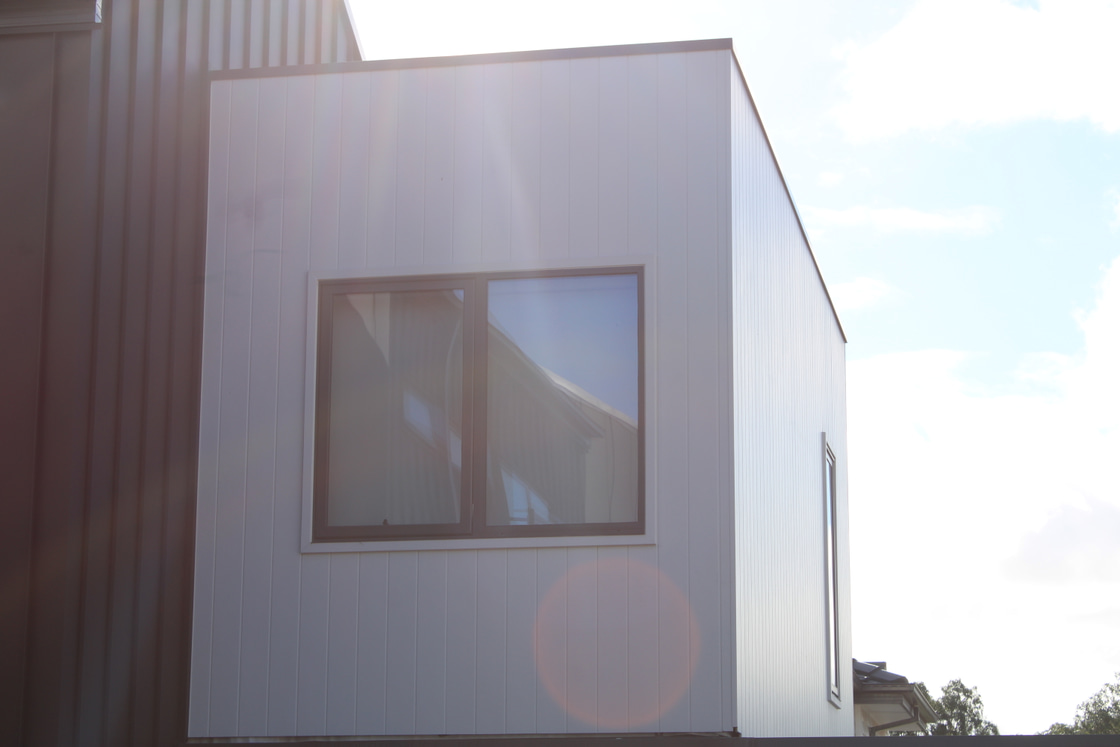 Sunlit James Hardie Axon facade with continuous vertical grooves across a long upper-storey wall
