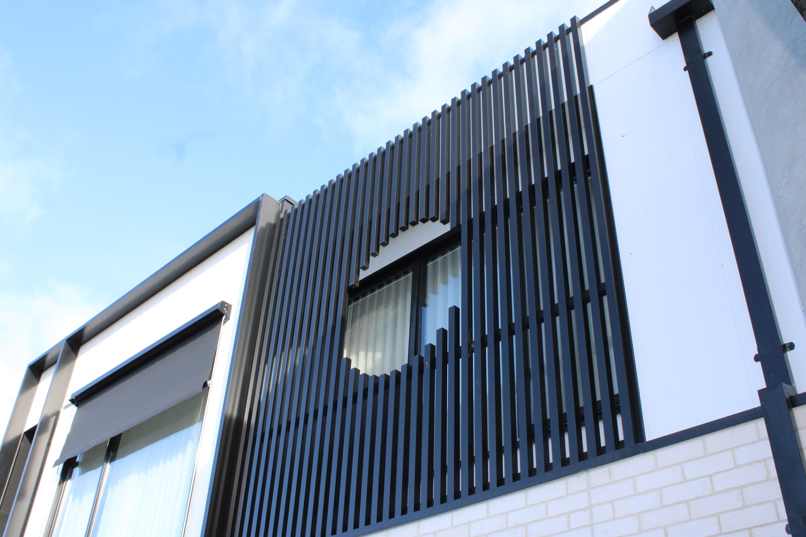 Custom circular opening formed through individual black aluminium battens around an upper-storey window