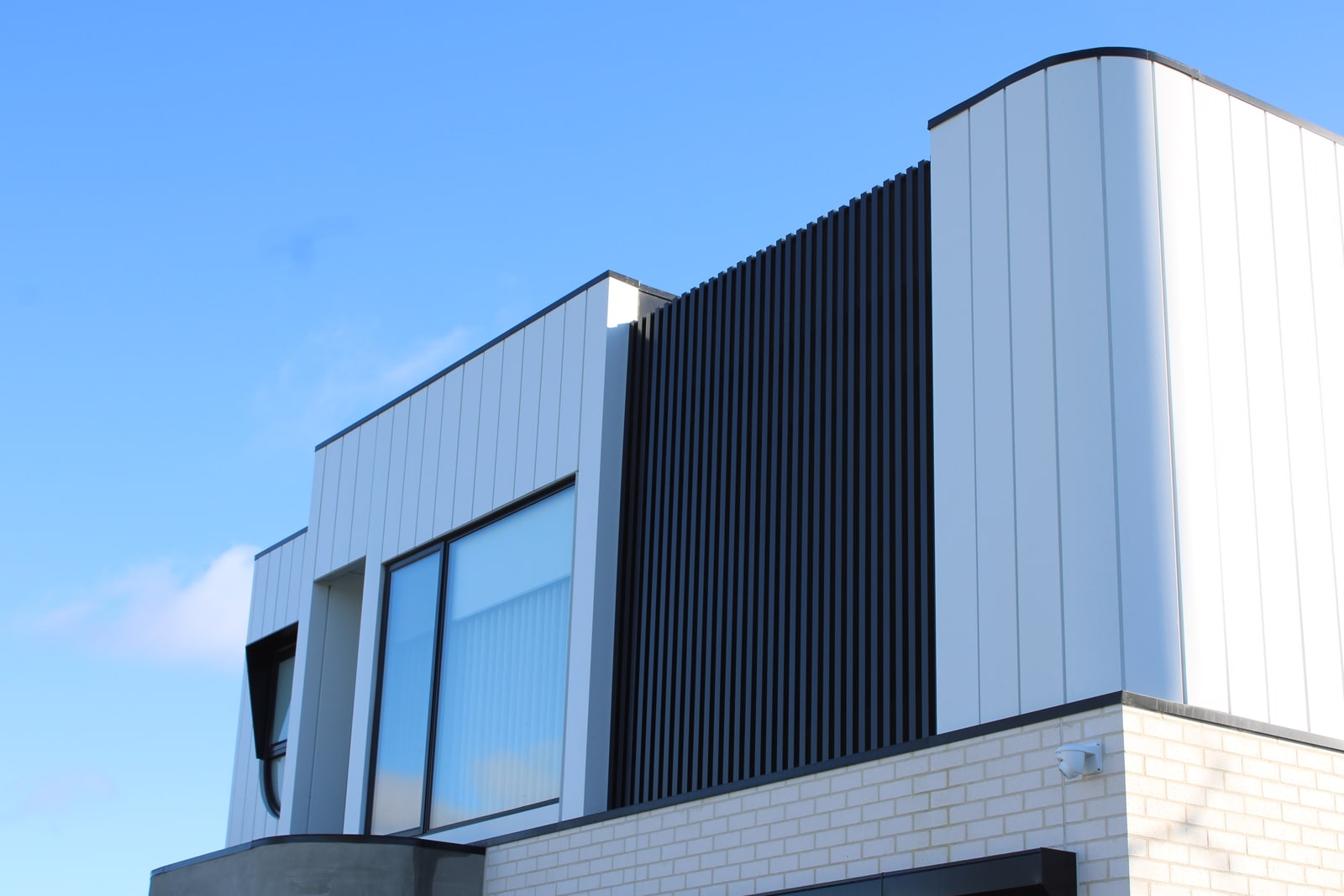 Full Melbourne townhouse facade with a black aluminium batten screen integrated between white cladding volumes