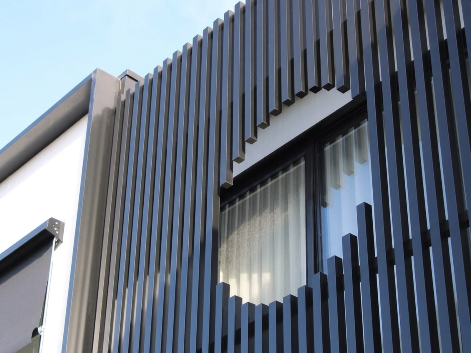 Black aluminium batten facade screen with a precisely formed circular opening around a window on a Melbourne home