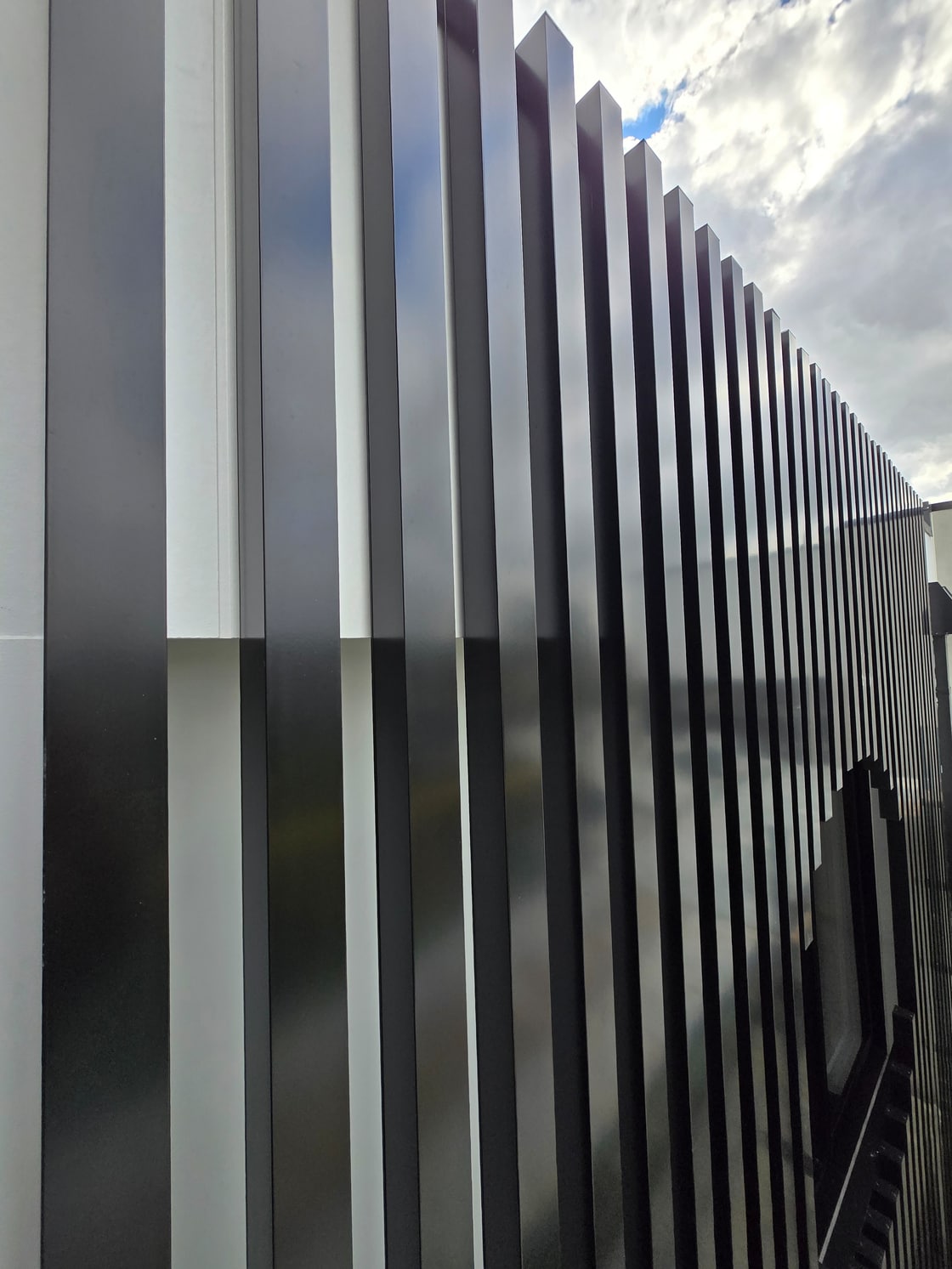 Oblique close-up showing the repeated depth and alignment of black aluminium facade battens