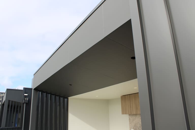 Charcoal soffit lining meeting timber-look cladding at an entry