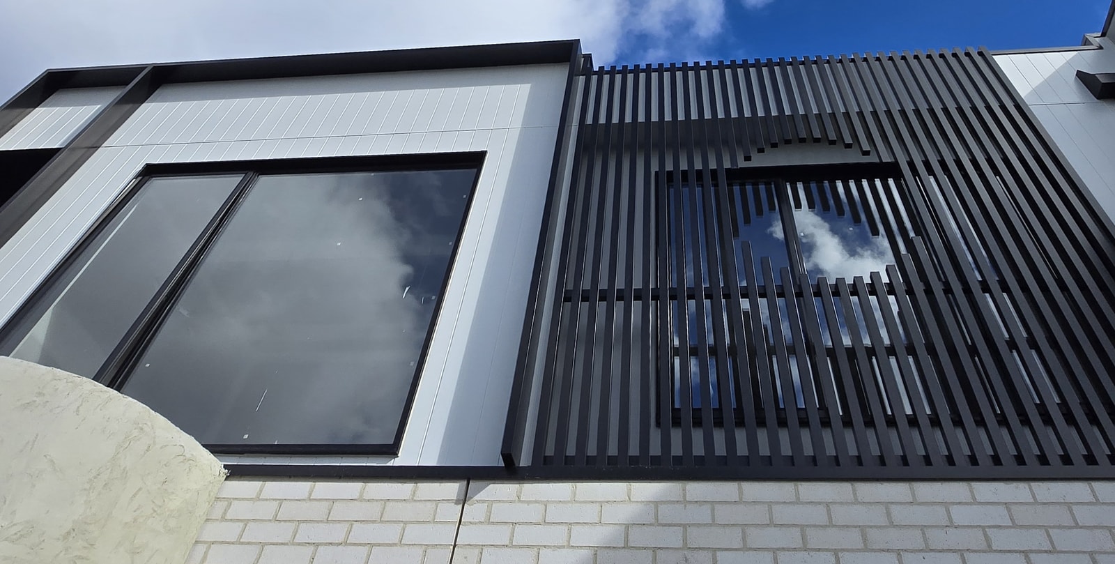 Custom black aluminium batten screen beside white vertically grooved facade cladding